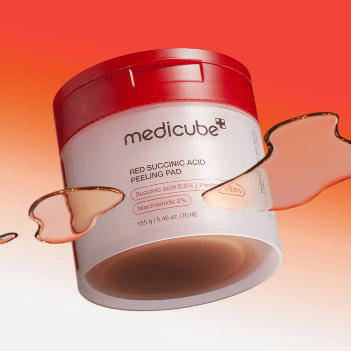 Medicube Red Succinic Acid Peeling Pad i en vit och röd burk, placerad mot en gradientbakgrund i rött och orange. Produkten innehåller succinic acid och niacinamid för exfoliering och hudförbättring. Flytande textur syns runt burken.