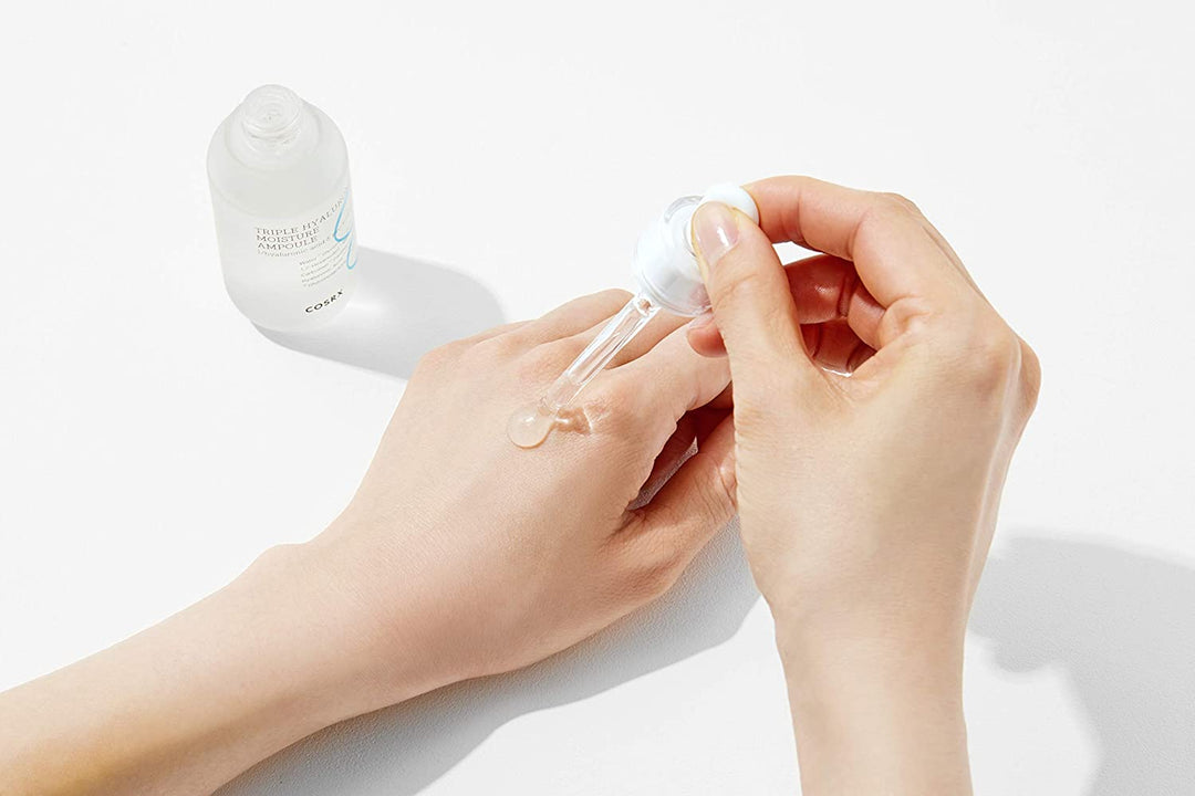 En hand som håller i en flaska COSRX Triple Hyaluronic Moisture Ampoule 40ml med hyaluronsyra och vitamin B5.