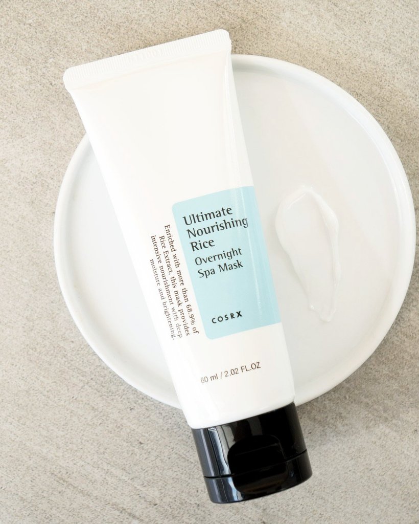 En tub Ultimate Nourishing Rice Overnight Spa Mask 60ml från COSRX sittande på en vit platta, designad för att ljusa upp huden.