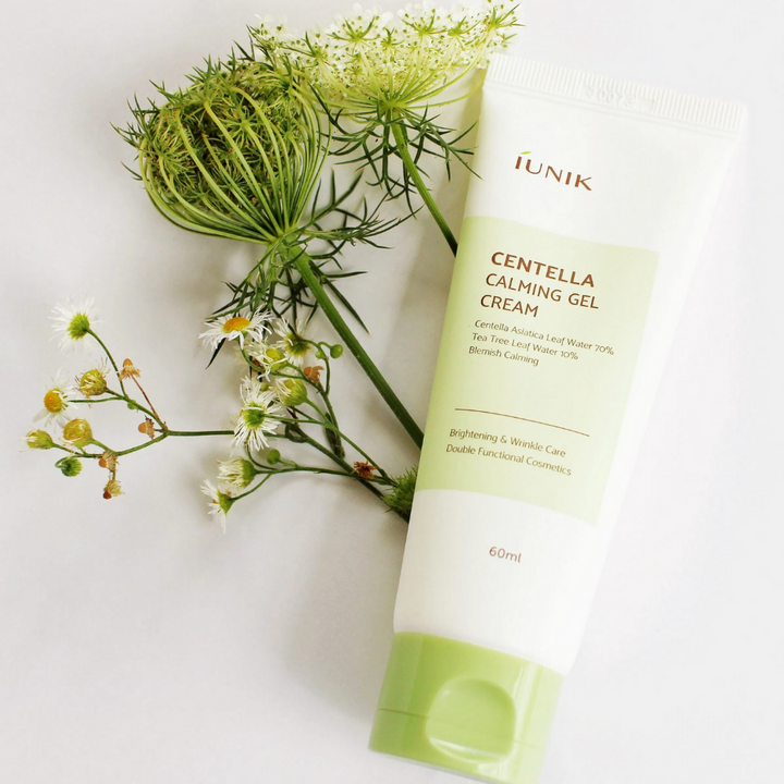 En tub iUNIK Centella Calming Gel Cream 60ml bredvid blommor.